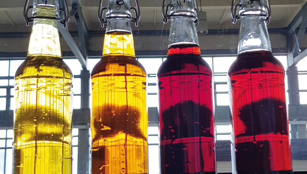 Four bottles containing monastery beers with different colors, ranging from pale yellow to dark red