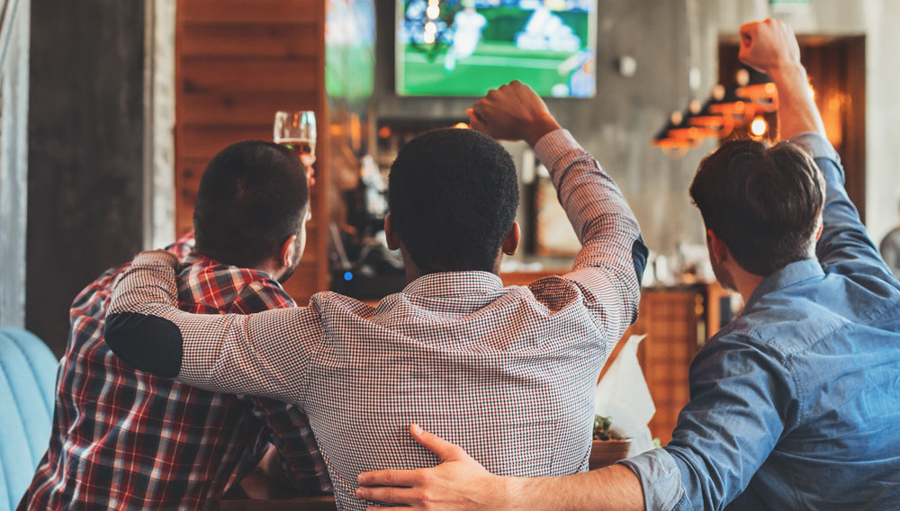 Three guys on a sofa watching the Super Bowl on TV (Source: iStock)