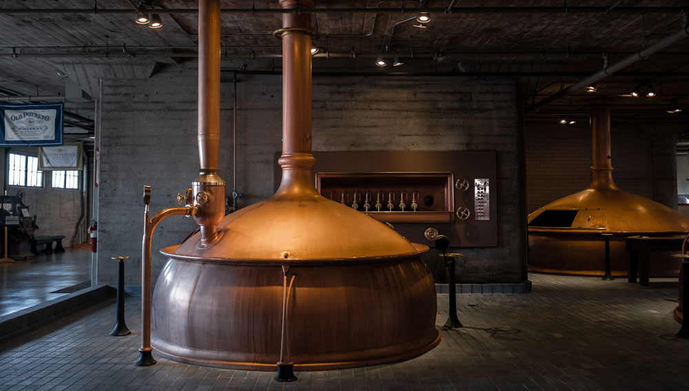 Copper brewing kettle in the spotlight against an unlit background (Photo: Claude Piché on Unsplash)