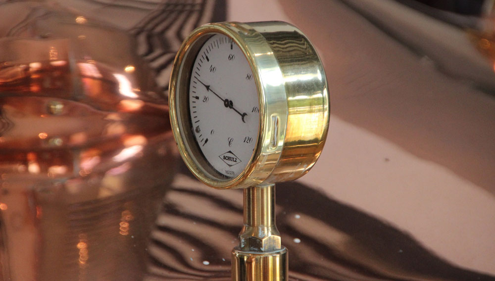 Analogue thermometer with white dial in front of a copper brewing kettle (Photo: Tom Builder on Pixabay)