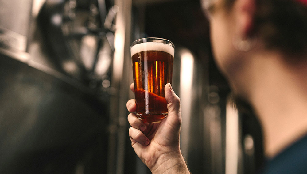 A person lifts a glass of beer in a brewery cellar and looks at it (Photo: Elevate on Unsplash)
