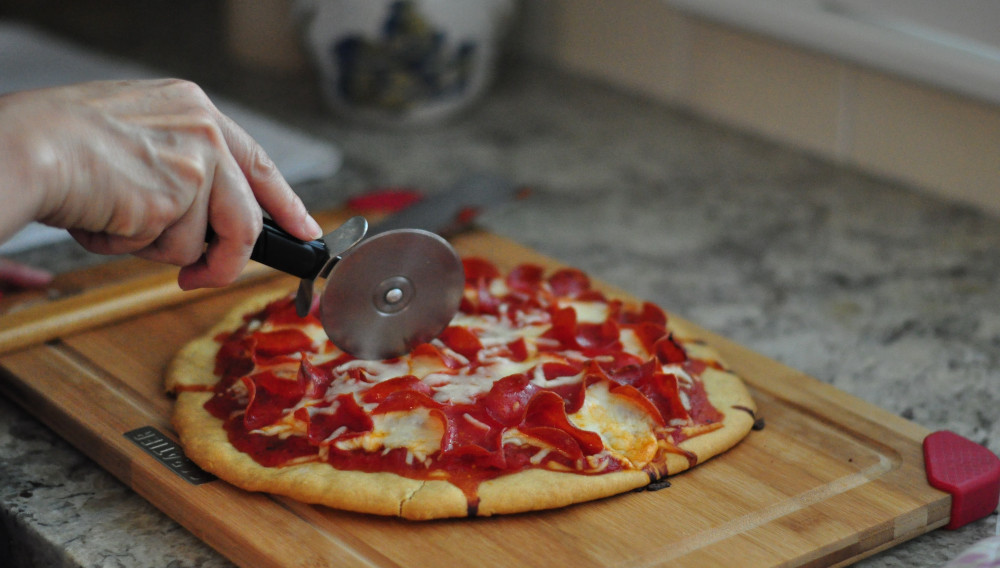 Person slicing pizza (Photo by Rosalind Chang on Unsplash)