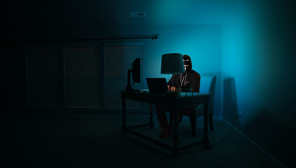 A man at a computer disguised as an anonymous hacker wearing a Guy Fawkes mask (Photo: Clint Patterson on Unsplash)