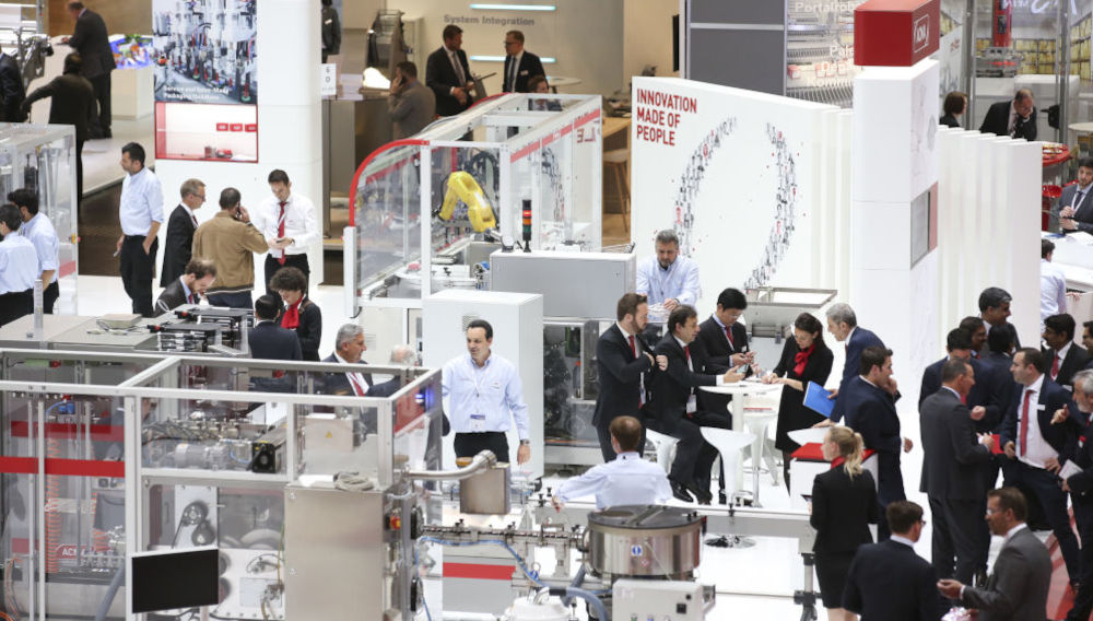 People in business suits talking to each other at a booth at interpack (Photo: Messe Düsseldorf)