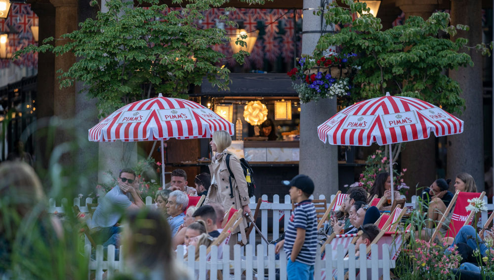 People sitting in front of a pub under umbrellas sporting the Pimm’s logo (Photo by Alexander London on Unsplash)