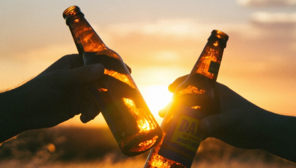 Two people toasting with beer bottles in front of a setting sun (Photo: Synergy PR)