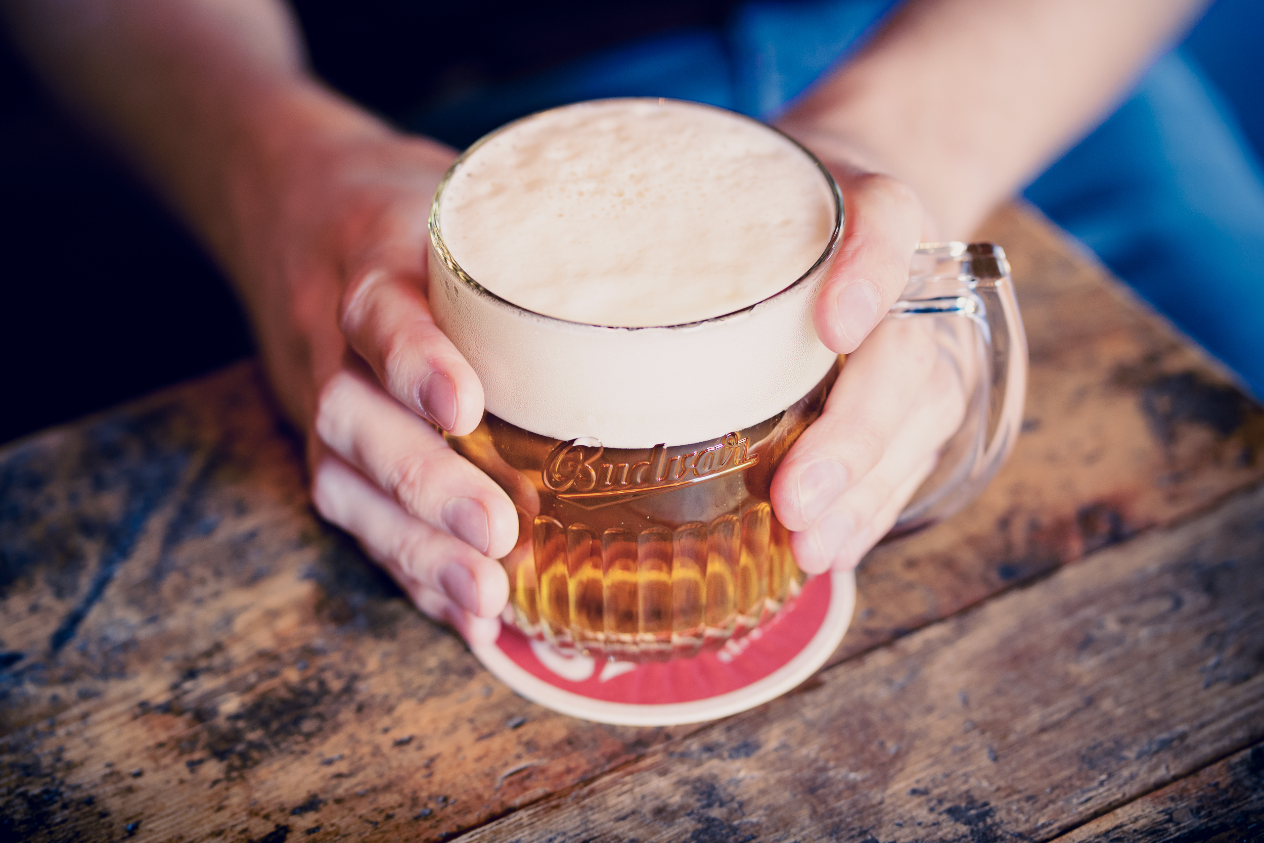 Two hands holding a glas of beer on a wooden table (Photo: Courtesy of Budweiser Budvar)