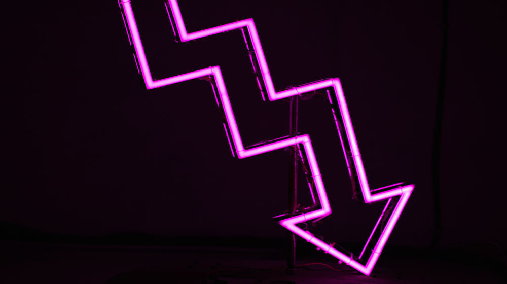 A neon arrow pointing downwards (Photo: Ussama Azam on Unsplash)