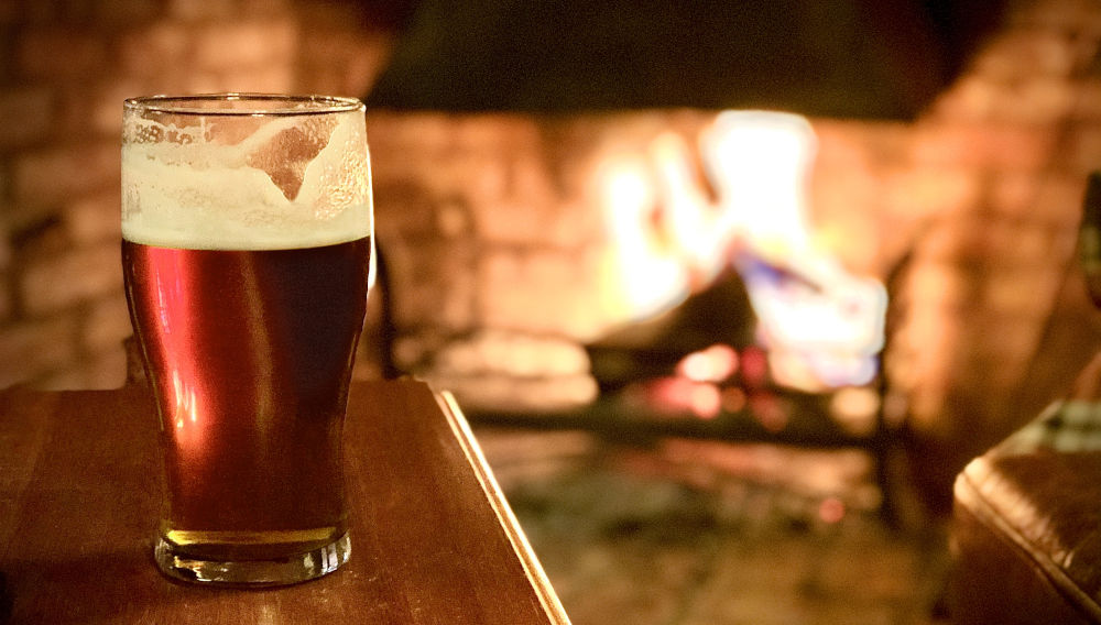 A glas of beer in front of a pub fire (photo Dan Barrett on Unsplash)
