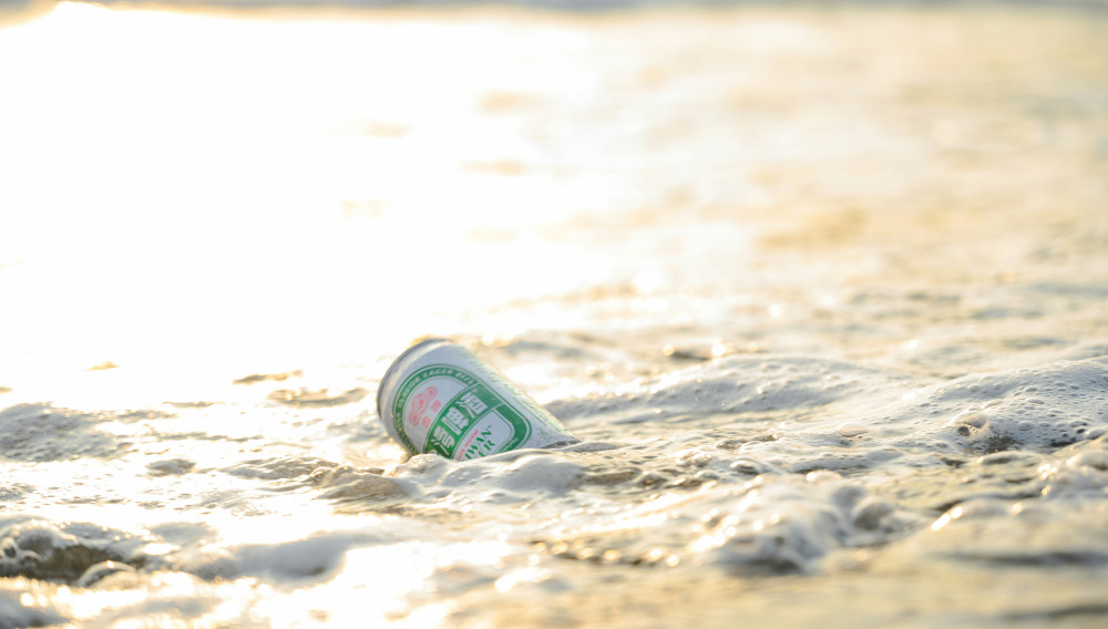 Beverage can on a sandy beach, with wave foam (Photo: vlog tottiy on Unsplash)