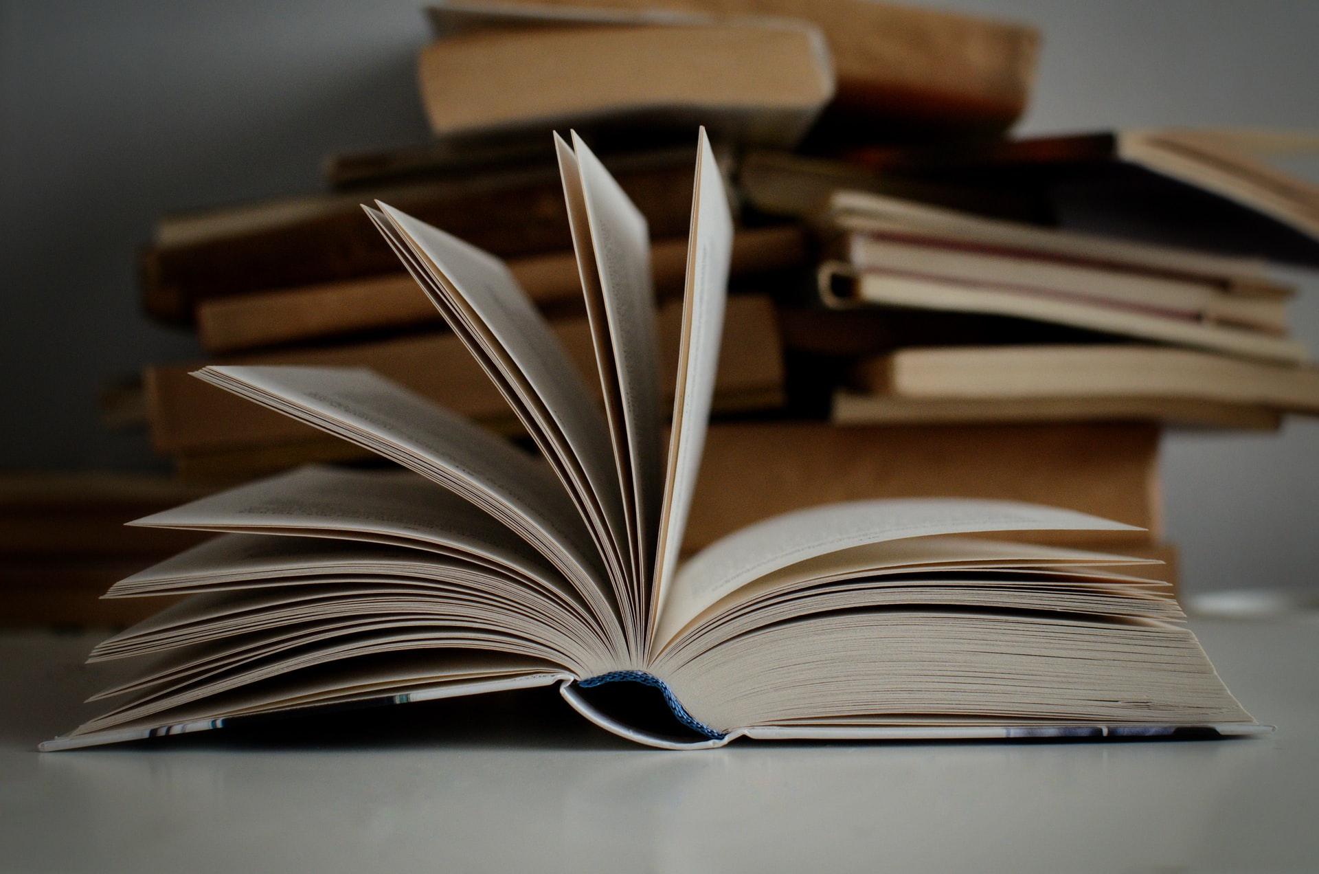 Open book in front of a stack of books (Photo: Mikolay on Unsplash)