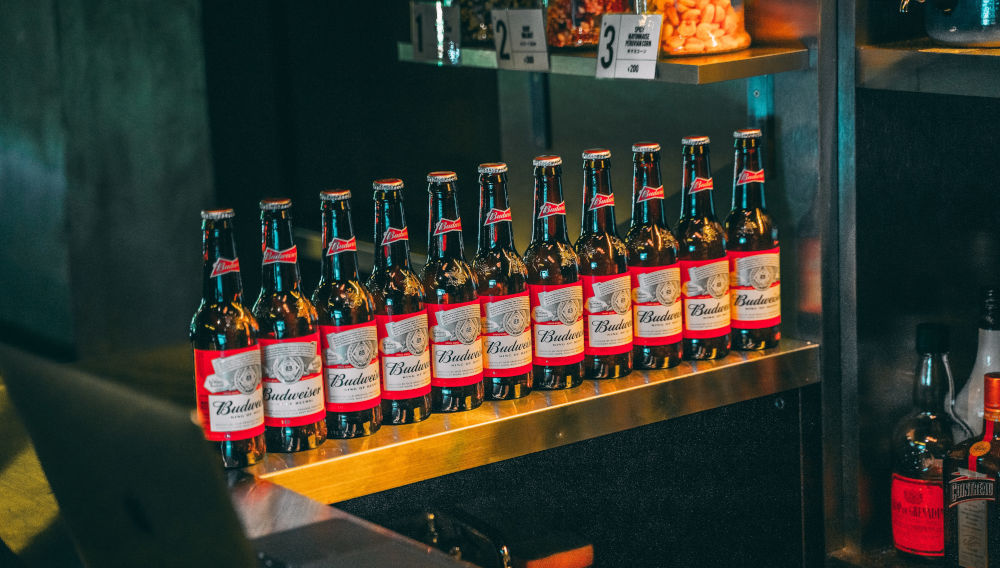 Budweiser bottles on a shelf (Photo by Heshan Perera on Unsplash)