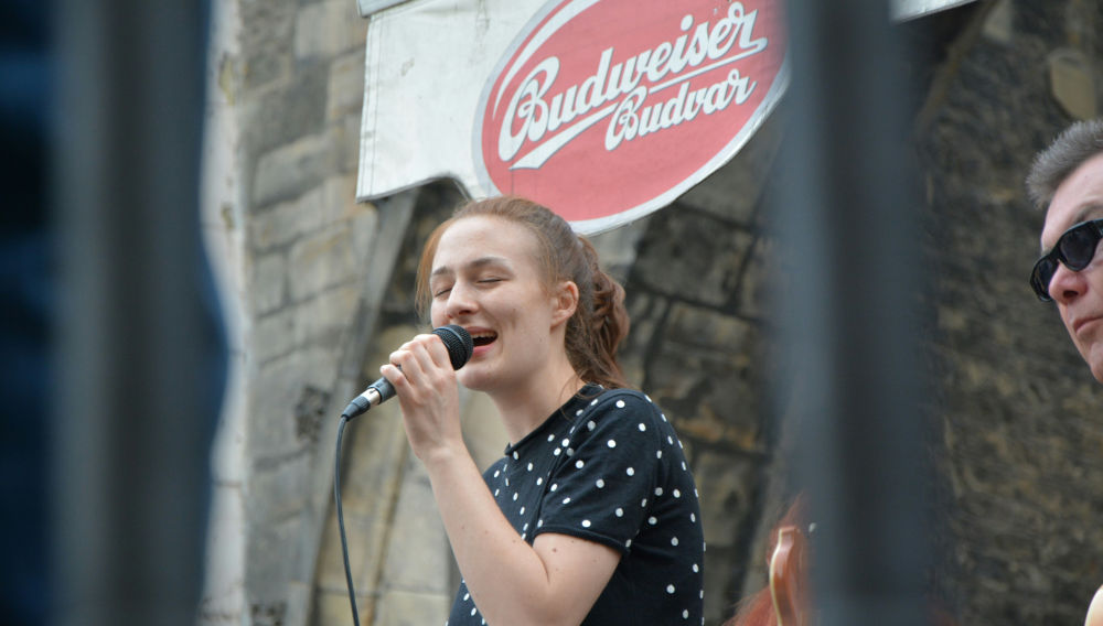 Singer in front of a wall with the Budweiser Budvar logo (Photo: Beth MacDonald on Unsplash)