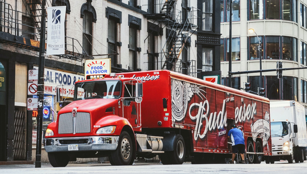 Red Budweiser trailer truck in front of concrete building (Photo by Maarten van den Heuvel on Unsplash)