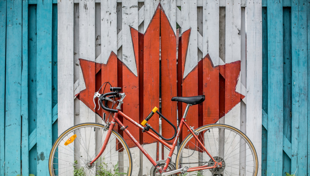 Bike in front of a light blue wall with a white square in the middle, surmounted by a red maple leaf (Photo: Ali Tawfiq on Unsplash)