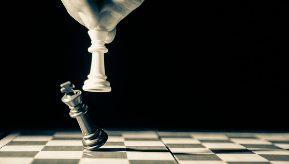 Hand hovering over a chess board holding the white king and pushing the black king over (Photo by GR Stocks on Unsplash)