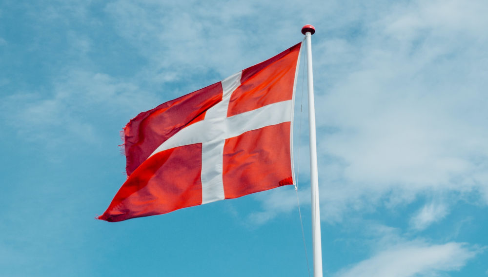 Danish flag against a blue sky (Photo by Markus Winkler on Unsplash)
