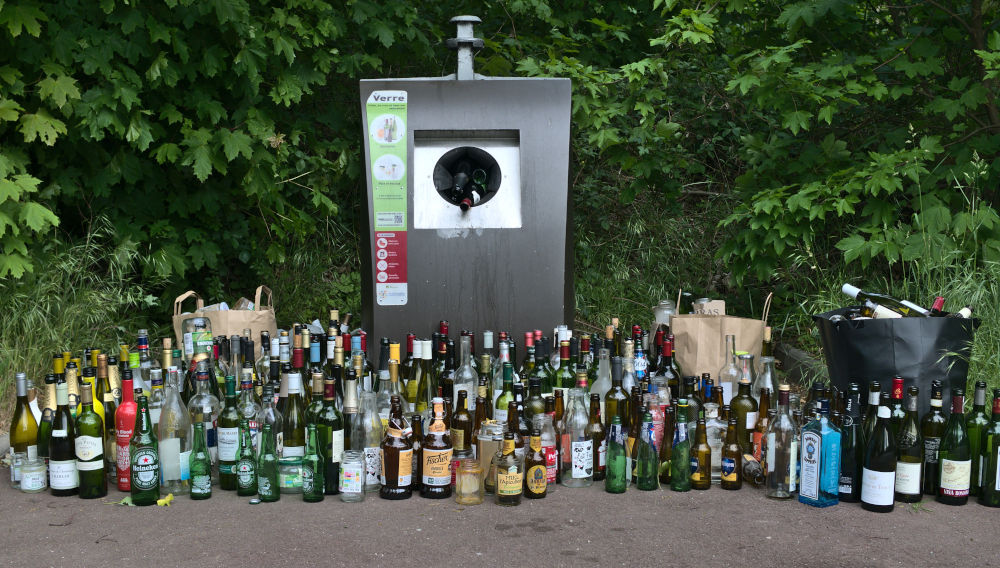 A lot of different empty glass bottles in front of an already full recycling container (Photo: Aleksandr Kadykov on Unsplash)
