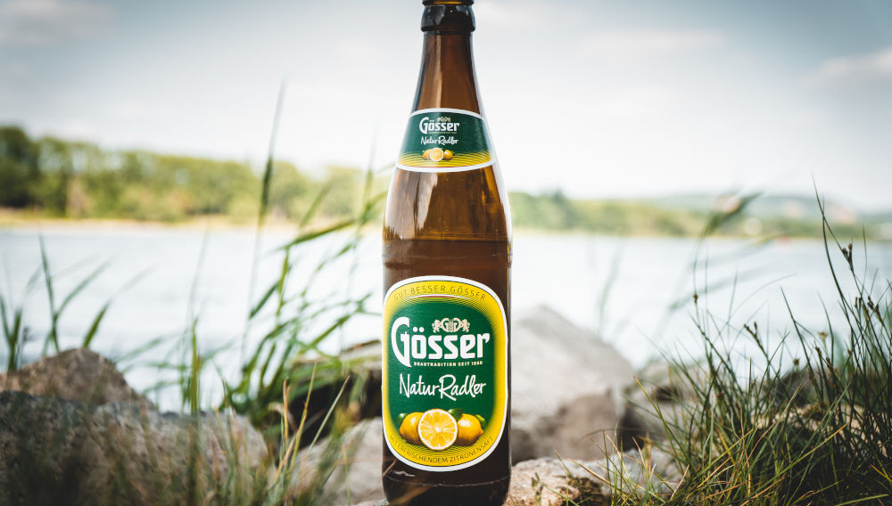 Braune Gösser Natur Radler-Flasche am Seeufer (Foto: Jonathan Kemper auf Unsplash)
