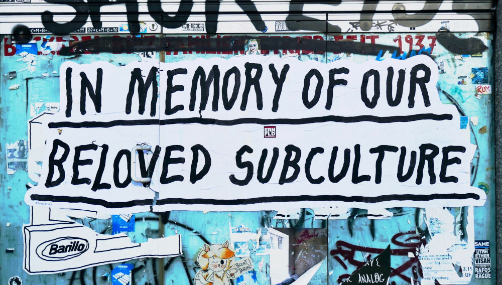 Graffiti in Cologne: Black and white tag on a colourful door saying, “In memory of our beloved subculture” (Photo by Bekky Bekks on Unsplash)