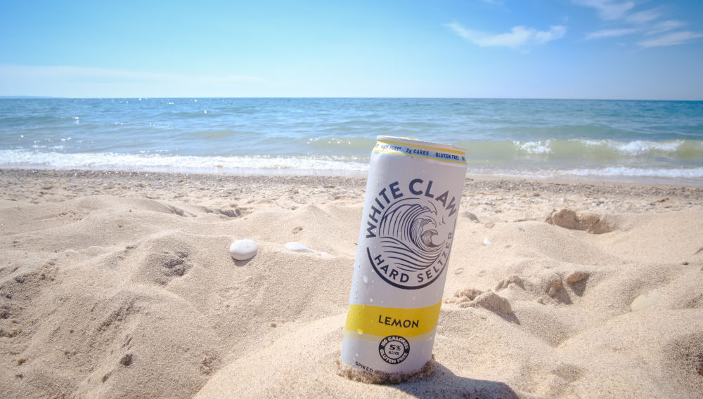 White and blue hard seltzer can in beach sand (Photo by Cyrus Crossan on Unsplash)