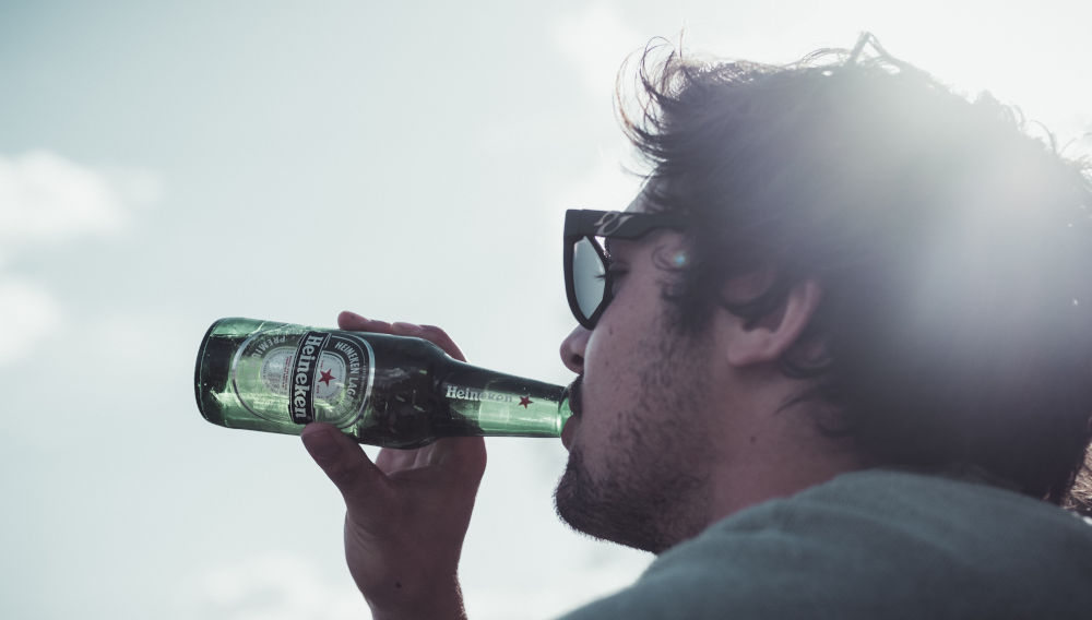 Person drinking from a green Heineken bottle (Photo by Daniel Wirtz on Unsplash)