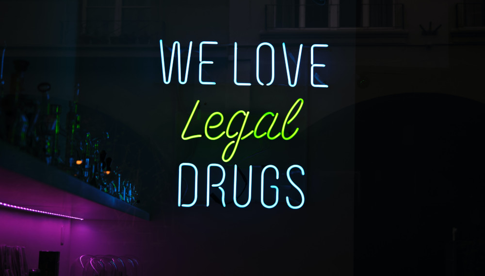 neon sign "we love legal drugs" (Photo: Simon Schwyter, Unsplash)