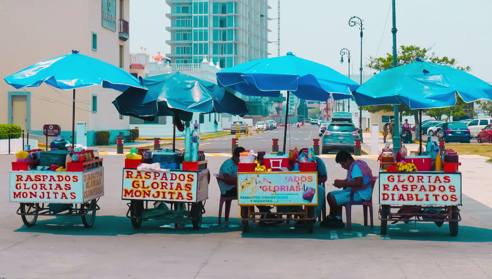 Bunte Marktstände unter blauen Sonnenschirmen, Mexiko (Foto von Roberto Carlos Roman Don auf Unsplash)