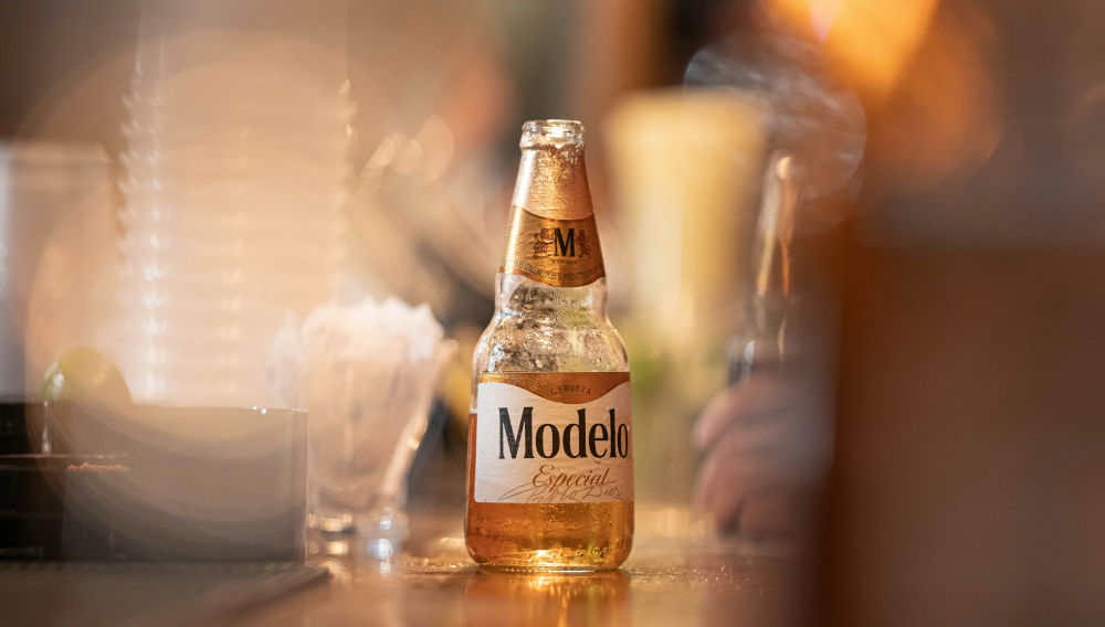 Close-up photo of a Modelo bottle on a bar table, against a blurry background (Photo: Hector Reyes on Unsplash)