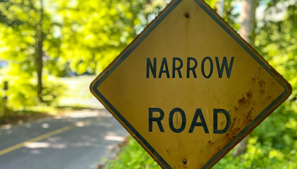 Yellow sign on an empty road, saying: Narrow road (Photo by Lance Grandahl on Unsplash)