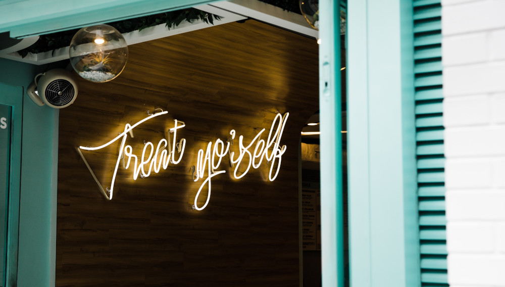 Neon sign saying “treat yourself” (Photo by Jenna Day on Unsplash)