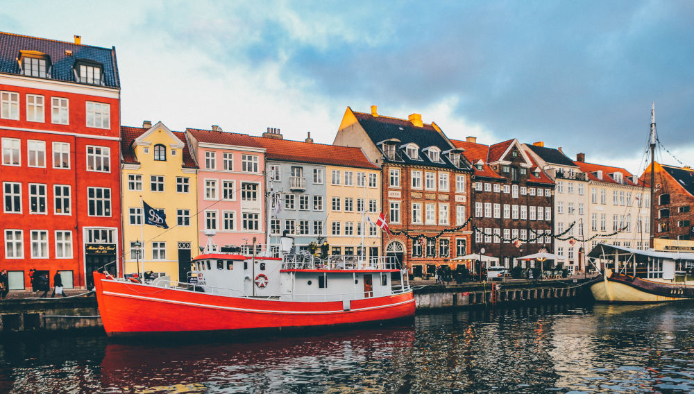 Boats on a river flowing through Nyhavn, with picturesque colourful houses in the background (Photo by Nick Karvounis on Unsplash)