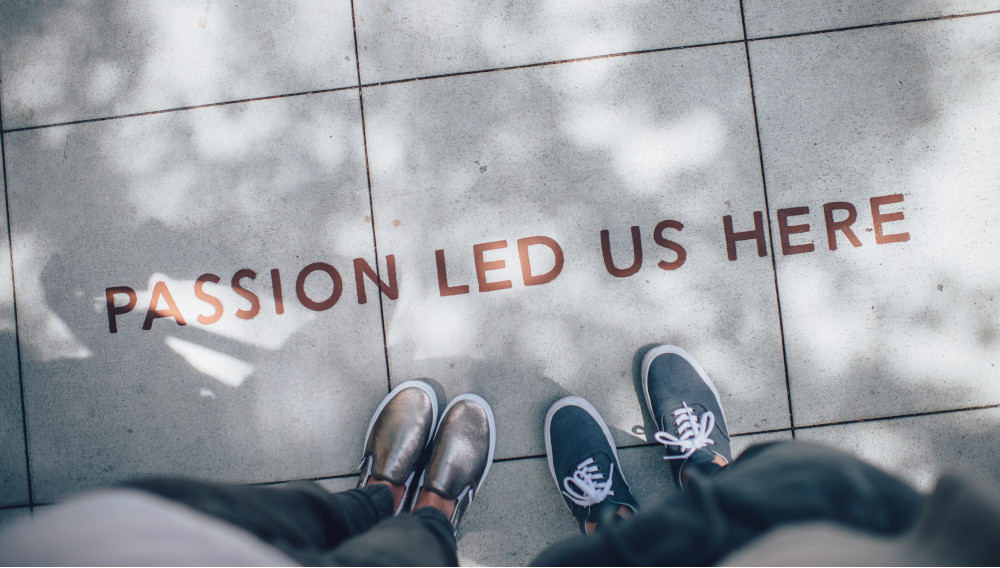 "Passion led us here" written on the floor, two pairs of shoes standing in front of it (Photo: Ian Schneider, Unsplash)