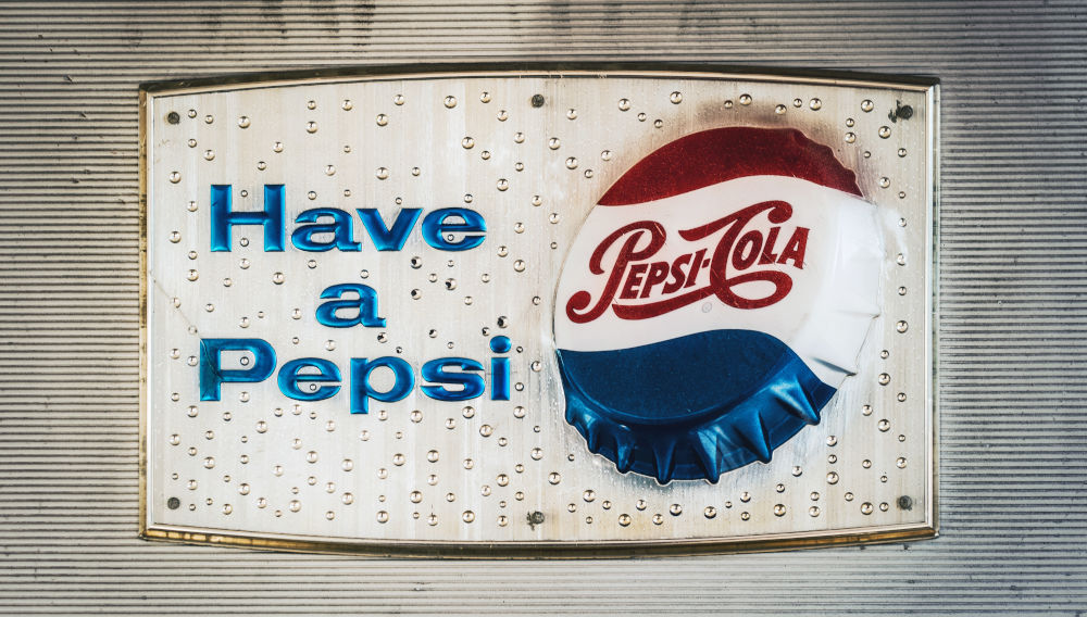 Advertising sign depicting a PepsiCo bottle cap and blue letters saying: “Have a Pepsi” (Photo by Tim Mossholder on Unsplash)