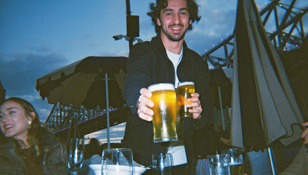 Person holding two beer glasses and smiling (Photo by Mark Broadhead on Unsplash)