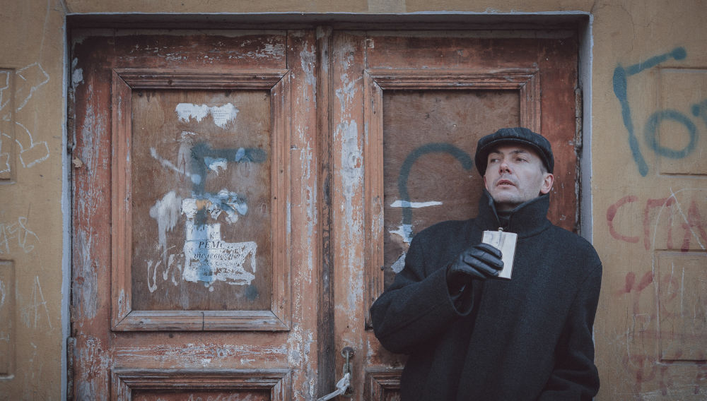 Person holding a hip flask, standing in front of a wooden door sprayed with graffiti (Photo by Mihail Tregubov on Unsplash)