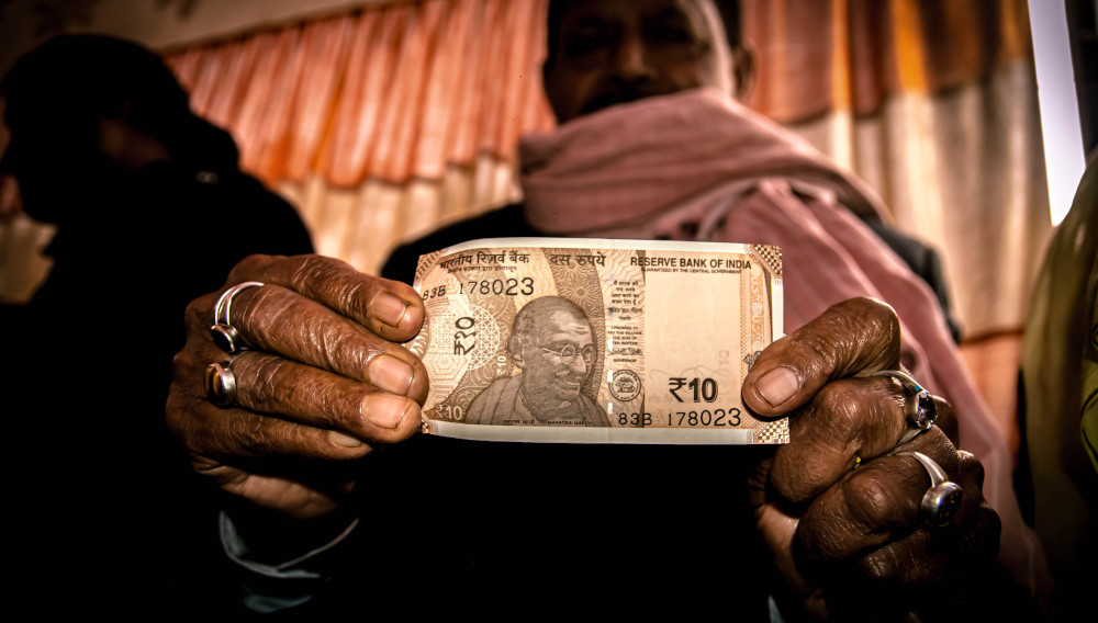 A man holding a rupee bank note into the camera (Photo: Deepal Tamang, Unsplash)