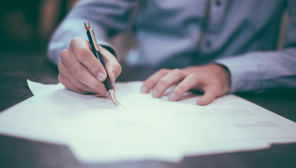 Person signing a piece of paper (Photo: Scott Graham on Unsplash)