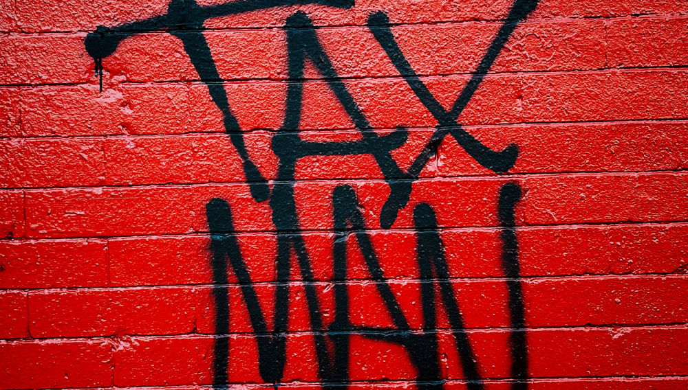 Graffiti Tax Man on red brickwall (Photo: Jon Tyson on Unsplash)