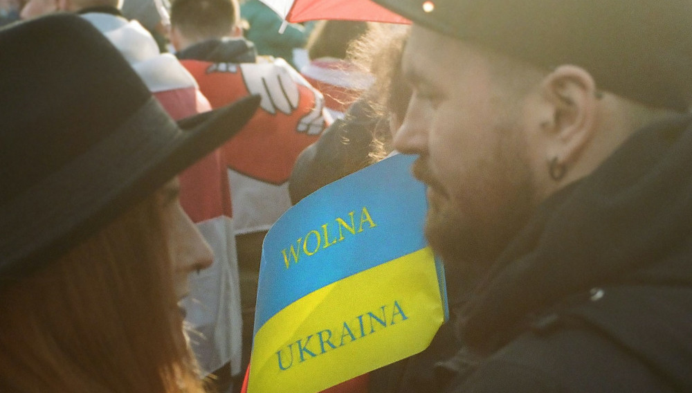 Two people in a crowd holding a blue and yellow flag saying “Free Ukraine” (Photo by Jana Shnipelson on Unsplash)