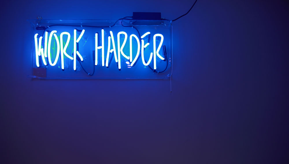Blue neon sign, saying: “Work harder” (Photo by Jordan Whitfield on Unsplash)