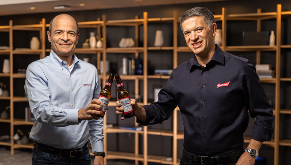 Michel Doukeris (re.) und Carlos Brito stoßen mit zwei Flaschen Bier an