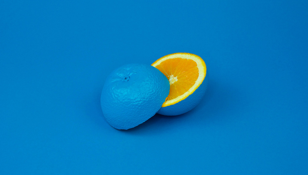 Orange mit blau gefärbter Schale vor blauem Hintergrund (Foto: davisuko auf Unsplash)