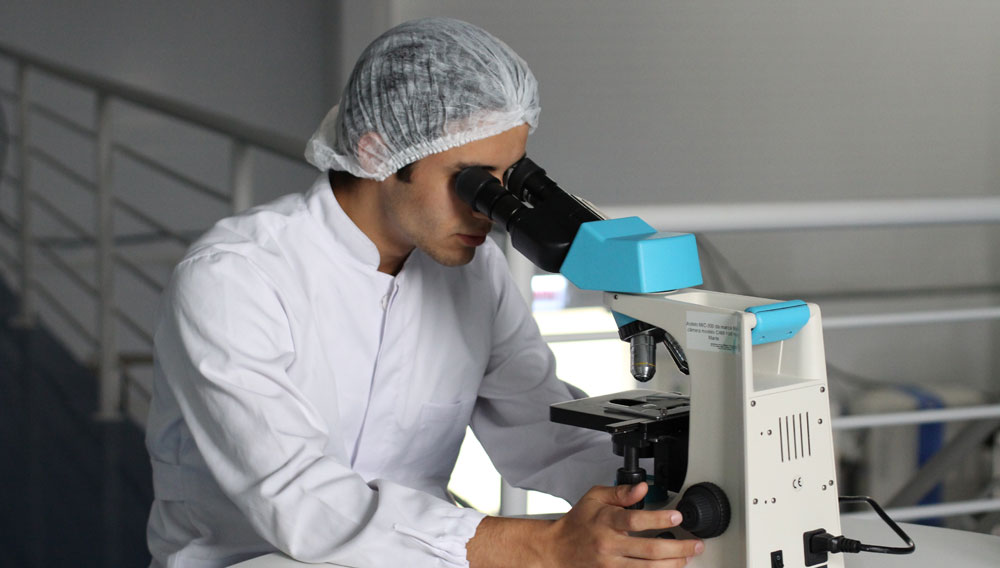 Mann in weißem Kittel arbeitet an einem Mikroskop