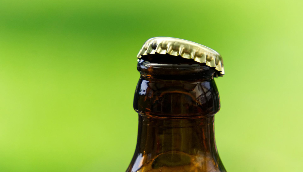 Bierflasche mit gelöstem Kronkorken vor grünem Hintergrund (Foto: Markus Distelrath auf Pixabay)
