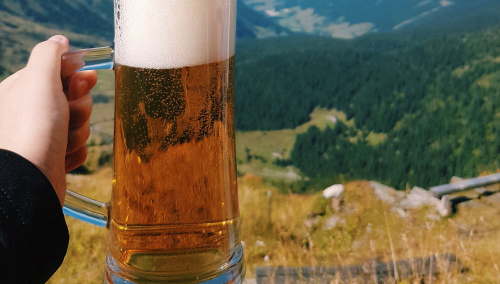 Krügerl Bier vor Berglandschaft (Foto: Reiseuhu auf Unsplash)