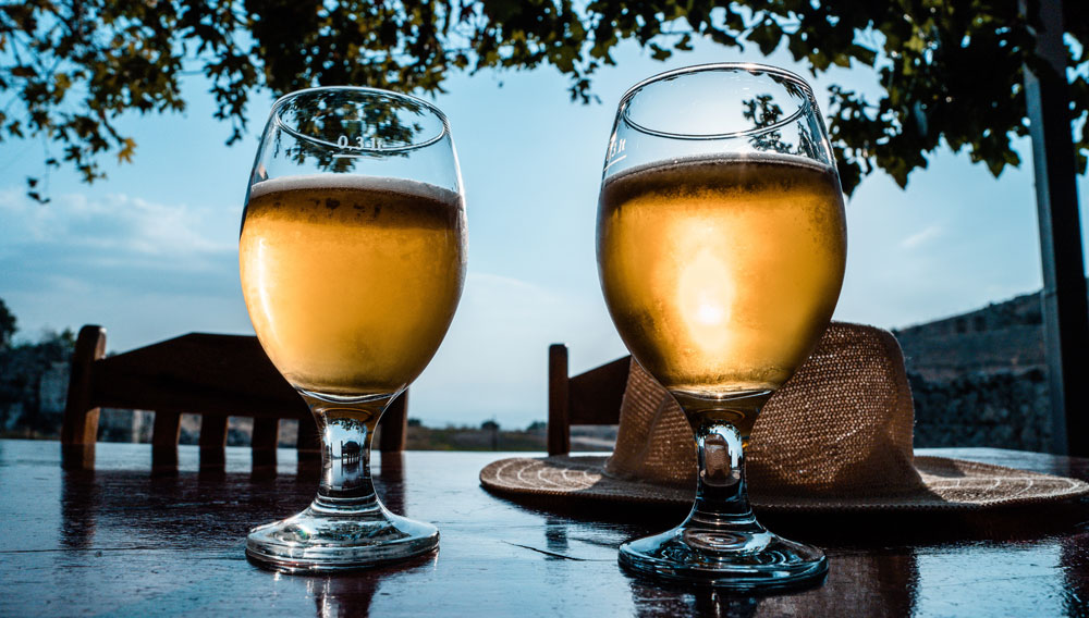 Zwei Biergläser auf einem Tisch im Freien mit Strohhut (Foto: Ümit Yıldırım auf Unsplash)