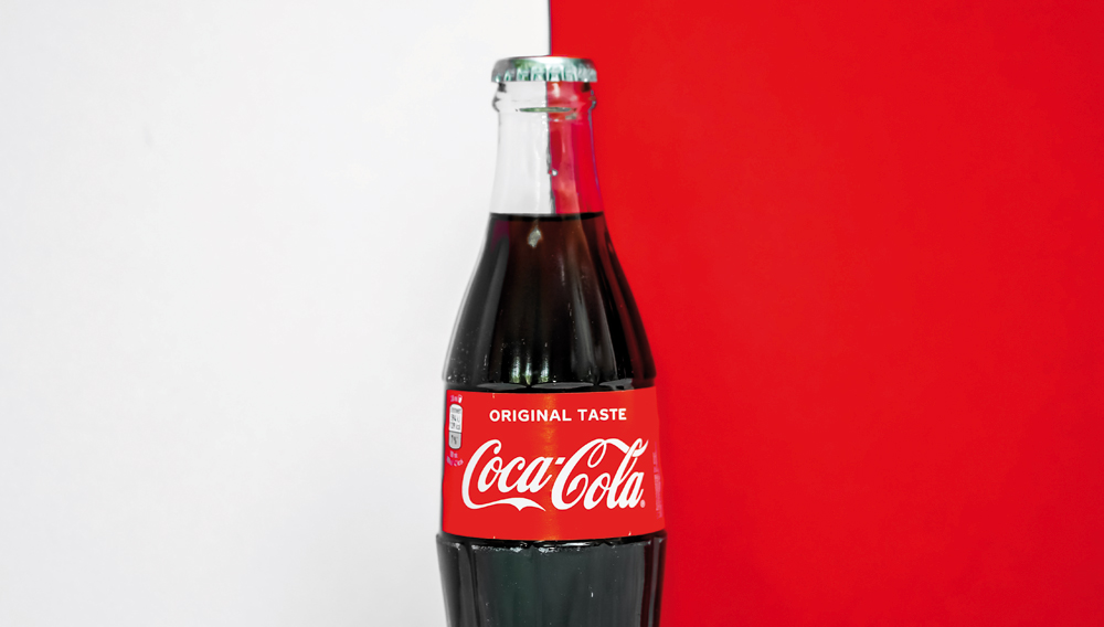 Coca Cola Flasche vor weiß-rotem Hintergrund (Foto: Laura Chouette auf Unsplash)