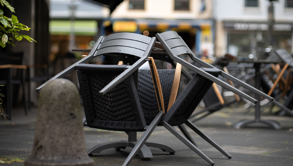Hochgestellte, leere Stühle im Außenbereich eines Cafes (Foto: Mika Baumeister auf Unsplash)