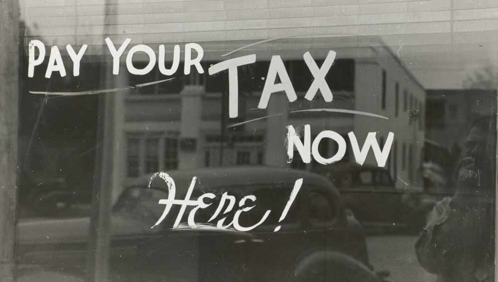Handgeschriebene Aufforderung auf einem Schaufenster: „Pay your Tax now Here!“ (Foto: The New York public library auf Unsplash)